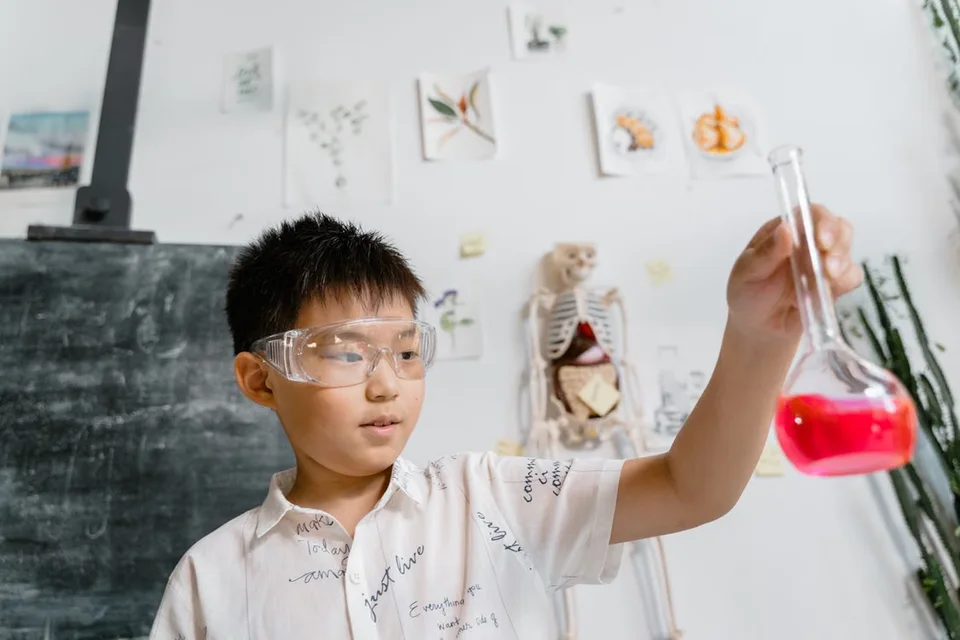 Niño con gafas de protección observando un matraz con líquido rosa